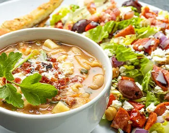 Bowl of soup garnished with parsley and chili flakes, served with a Mediterranean salad for the new Pranzo lunch pairings.
