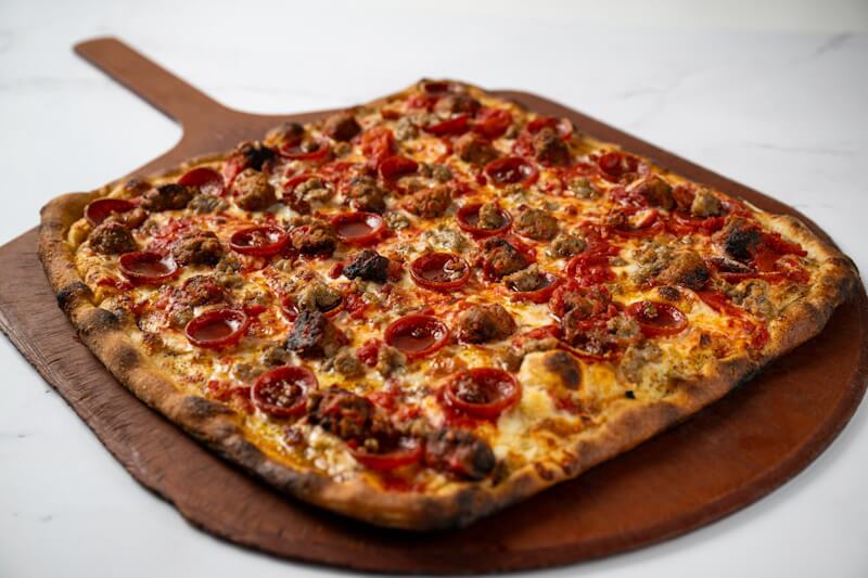 A large rectangular coal fired pizza loaded with pepperoni, sausage, and crumbled meatballs at Anthony’s Coal Fired Pizza.