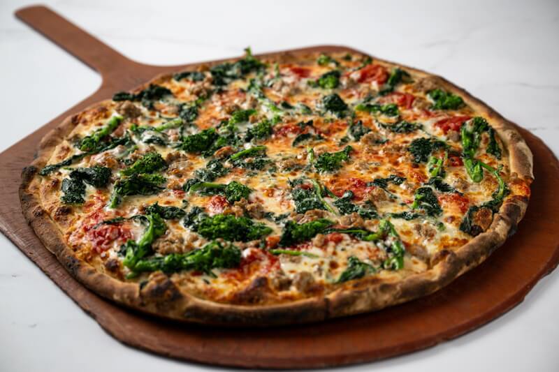 Coal fired pizza topped with crumbled sausage and tender broccoli rabe, a savoury and smoky pairing with bold Italian-style flavor.