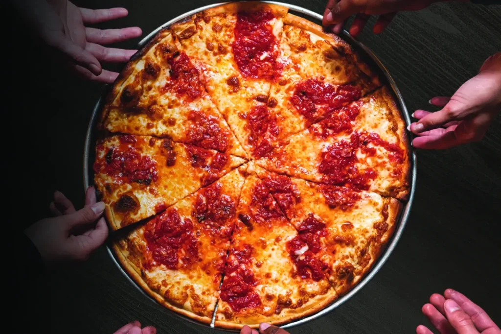 Hands reaching for coal fired cheese pizza at Anthony’s Coal Fired Pizza, promoting $10 pizza specials for National Pizza Day.