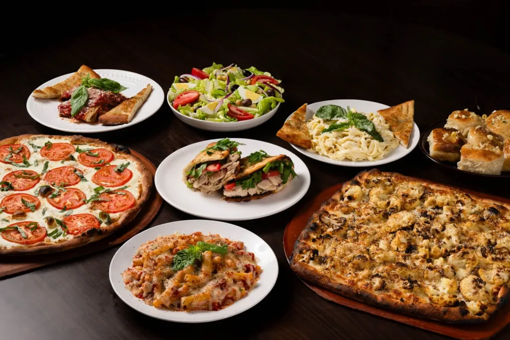 A variety of Italian appetizers, including pizza, salad, pasta, bruschetta, and stuffed bread, on a wooden table.