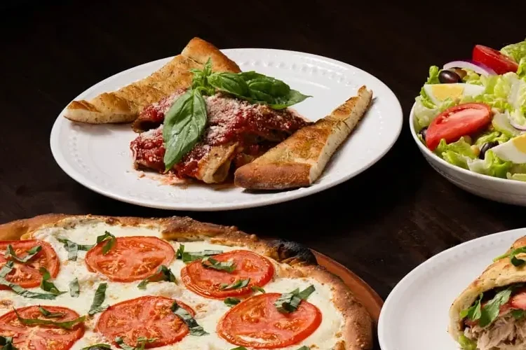 A variety of Italian appetizers, including pizza, salad, pasta, bruschetta, and stuffed bread, on a wooden table.