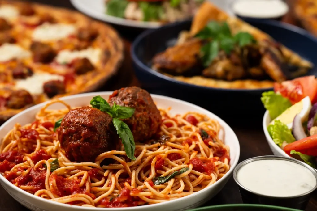 Sphagetti pasta with meatballs and pizza in the background.