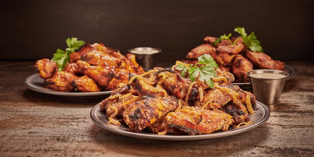 Grilled chicken wings with onions and fresh herbs served on metal plates.