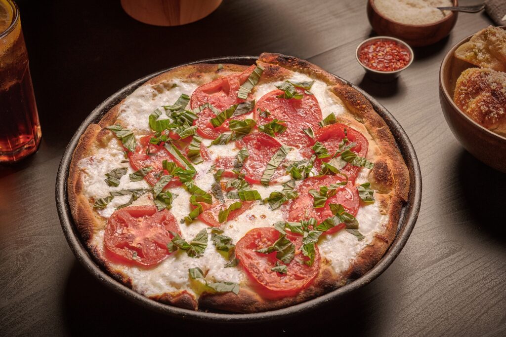 Coal-fired Margherita pizza with fresh mozzarella, sliced tomatoes, and basil on a crispy, charred crust.