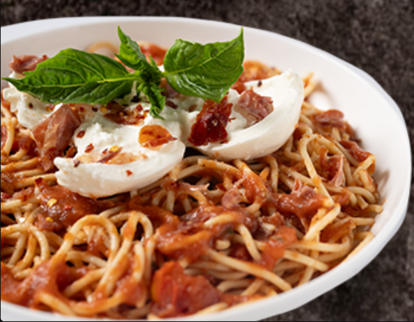 Spaghetti with marinara sauce, burrata cheese, prosciutto, chili flakes, and fresh basil in a white bowl.