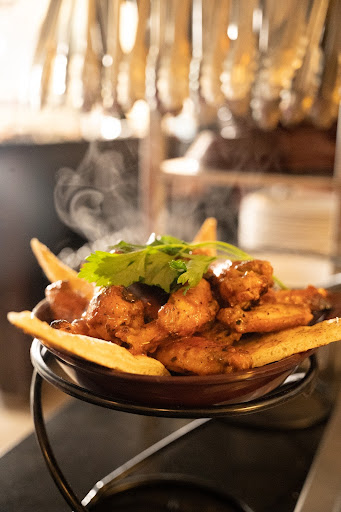 Steaming hot chicken wings with a rich sauce, garnished with cilantro and served with crispy fries.