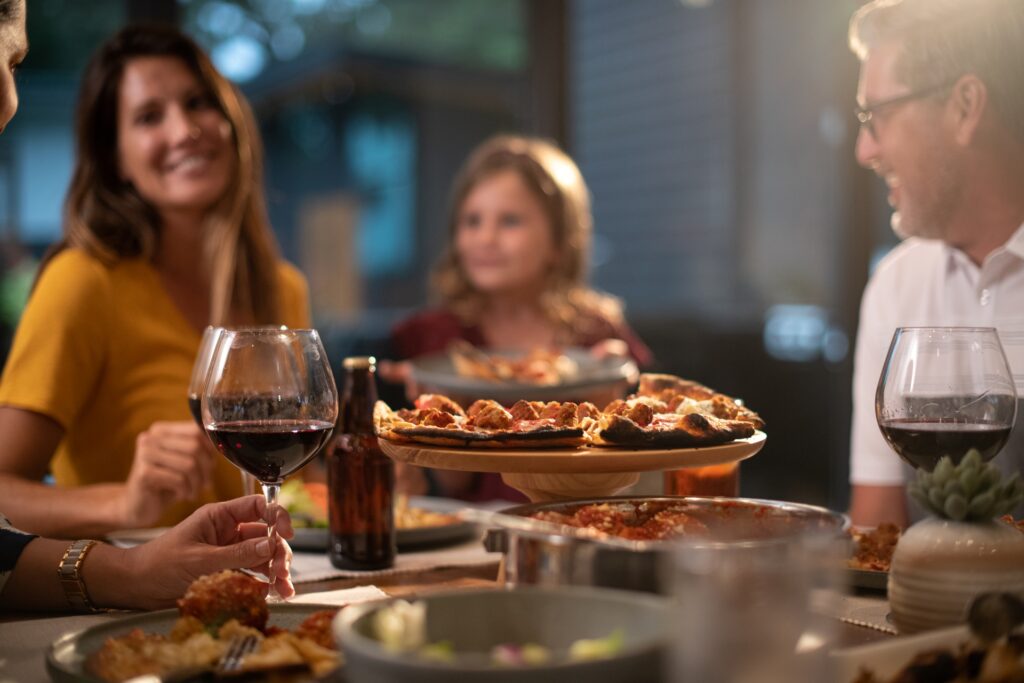 Family enjoying a dinner with meatball pizza, pasta, and wine at a warmly lit gathering.