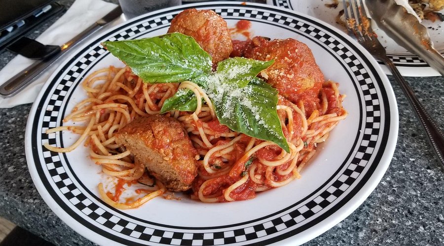 Spaghetti with marinara, meatballs, basil, and grated cheese on a checkered plate.