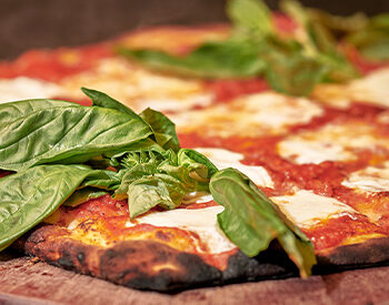 Wood-fired Margherita pizza with fresh basil, mozzarella, and tomato sauce.