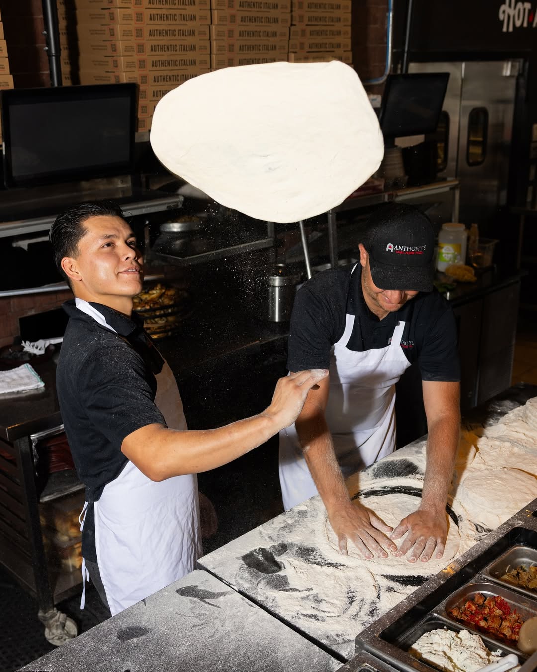 Two chefs at Anthony’s Coal Fired Pizza kneading pizza dough by hand, preparing authentic coal-fired crust.