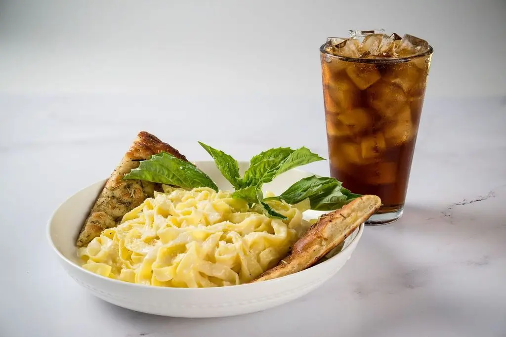 A bowl of pasta with meatballs, served with a cold Coke, for a comforting meal.