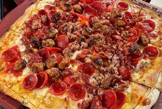 Topped Carnivori pizza beside garlic‑romano jumbo wings and twisted housemade garlic knots from Anthony’s.