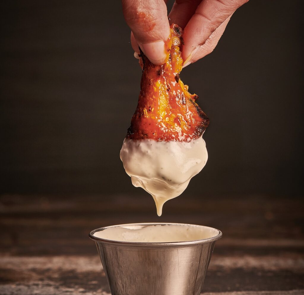 A person dips a coal oven-roasted chicken wing in Anthony’s signature dip.