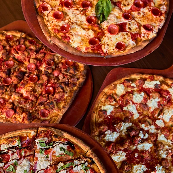 An overhead view of several pizzas on wooden trays, showcasing a variety of menu favorites.