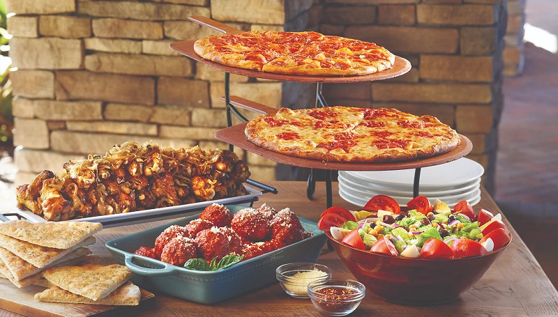 Anthony’s catering spread with coal-fired pizzas, wings, meatballs, salad, and focaccia on a table.