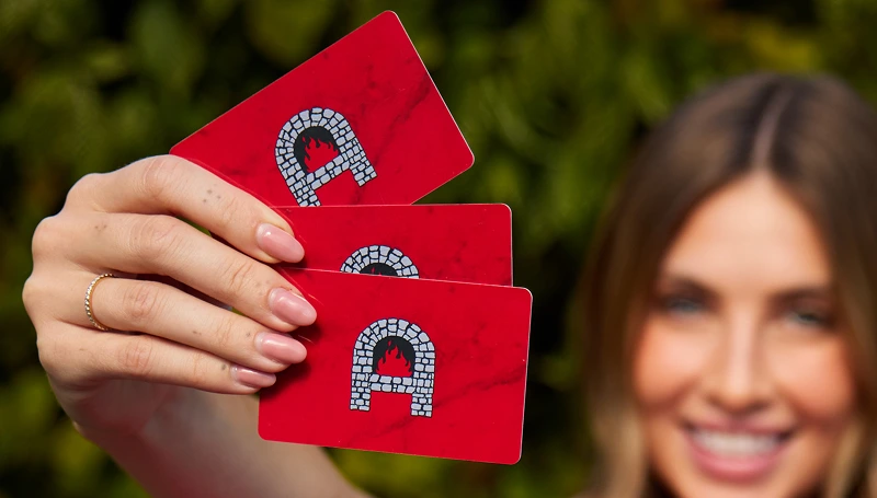 Guest holding Anthony’s gift cards over stacked red pizza boxes outside.