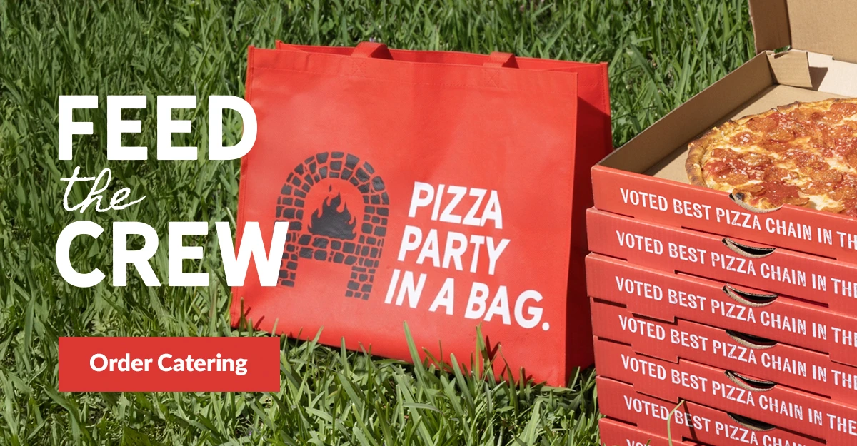Anthony’s Coal Fired Pizza catering bags and stacked pizza boxes on grass with “Feed the Crew” and “Order Catering” text.